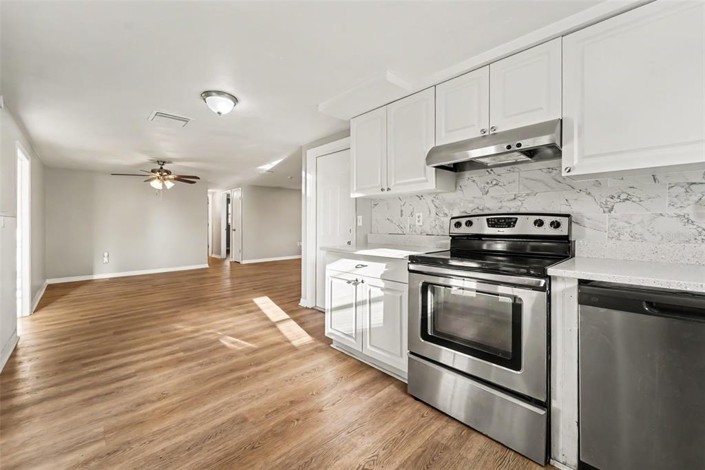 A kitchen with white cabinets and stainless steel appliances opens into a living area — 7207 SANDALWOOD DRIVE, PORT RICHEY, FL