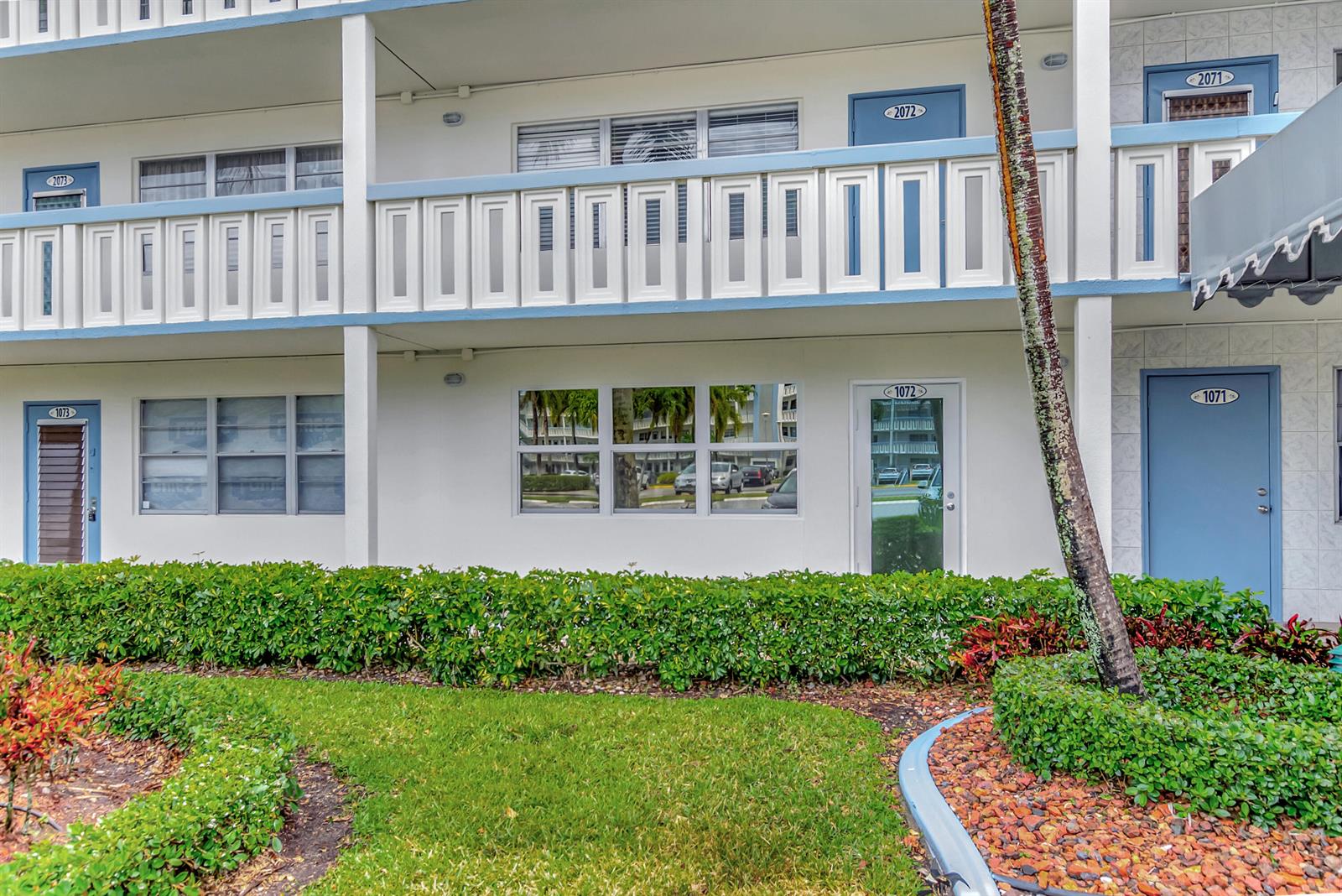 A two-story building exterior features blue doors, white railings, and a landscaped garden area — 1072 Yarmouth D, Boca Raton FL 33434, BOCA RATON, FL