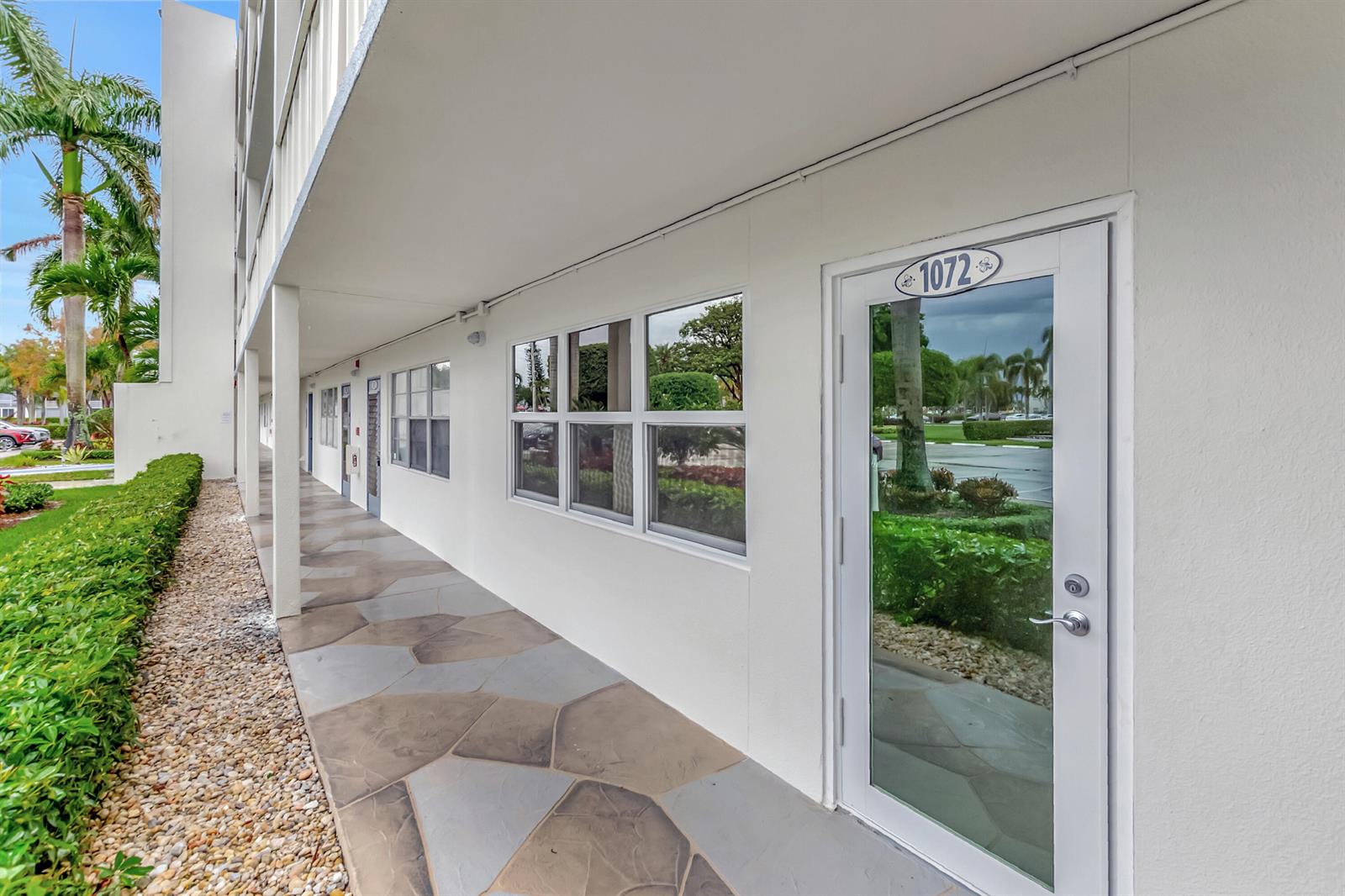 A white exterior building features a stone-tiled walkway, large windows, and a glass door — 1072 Yarmouth D, Boca Raton FL 33434, BOCA RATON, FL