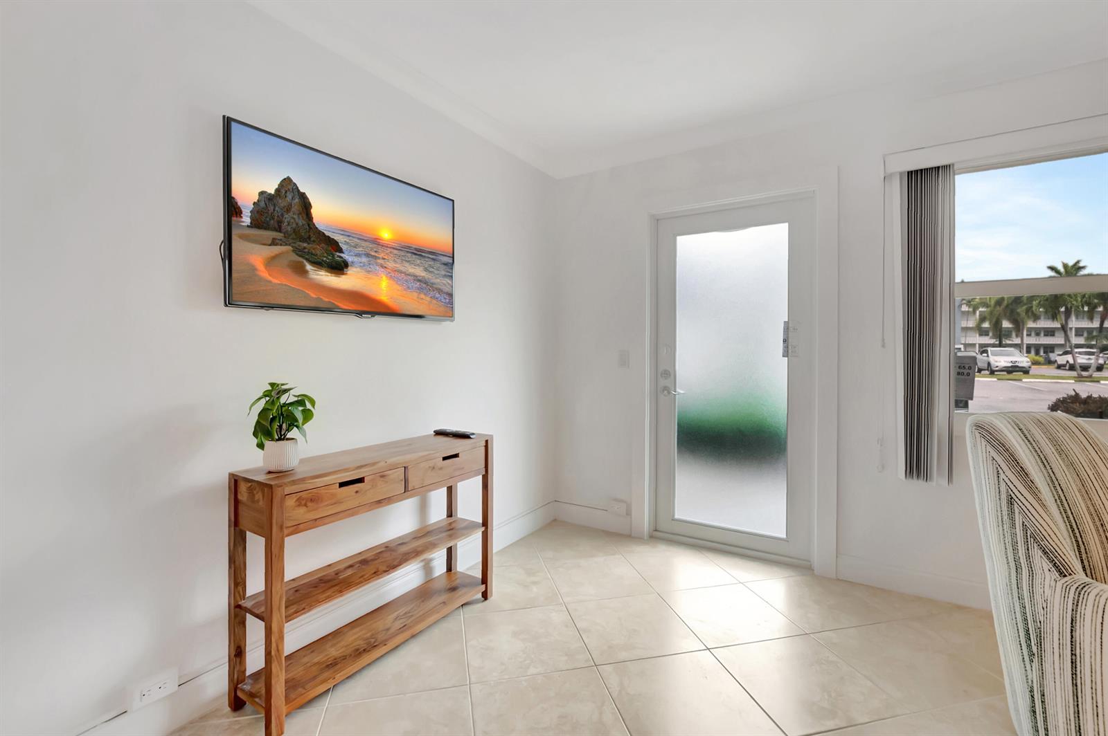 A bright room features a wall-mounted television, a wooden console table, and a glass door — 1072 Yarmouth D, Boca Raton FL 33434, BOCA RATON, FL