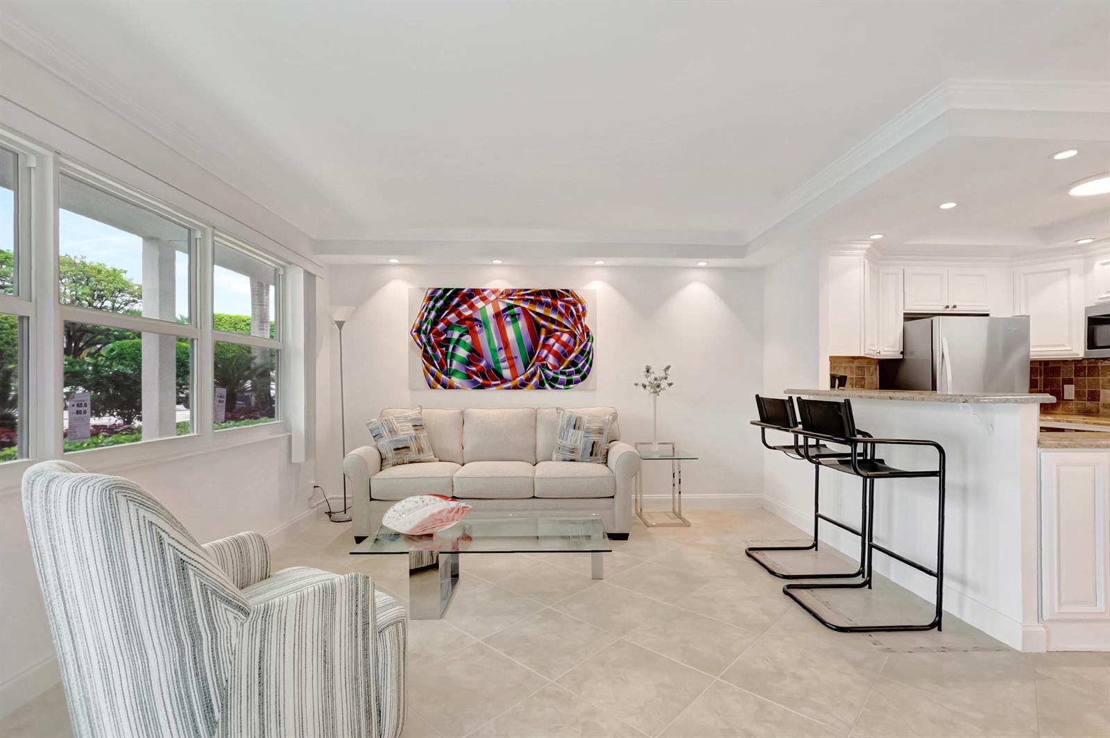 A living room with a sofa, striped armchair, glass coffee table, and an open kitchen — 1072 Yarmouth D, Boca Raton FL 33434, BOCA RATON, FL
