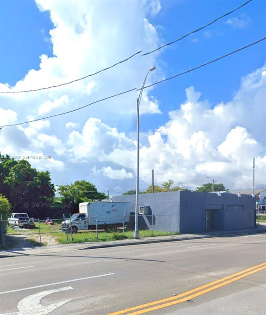 A gray commercial building stands next to a fenced vacant lot under a cloudy sky — 1222 NW 59th St, Miami FL 33142, MIAMI, FL
