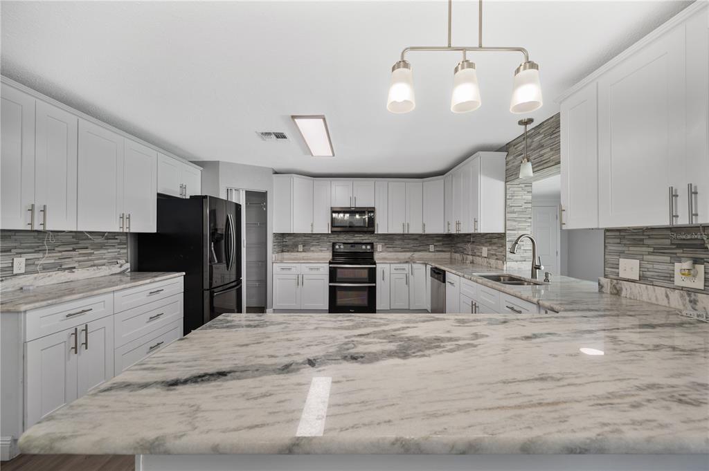 A kitchen features white cabinets, marble-patterned countertops, a stone backsplash, and black appliances — 510 WINDERMERE DRIVE, LAKELAND, FL