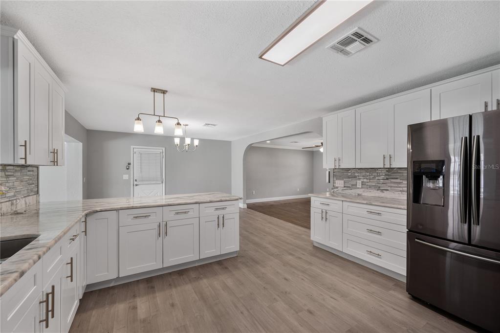 A modern kitchen features white cabinets, marble-look countertops, stainless steel appliances, and light wood flooring — 510 WINDERMERE DRIVE, LAKELAND, FL