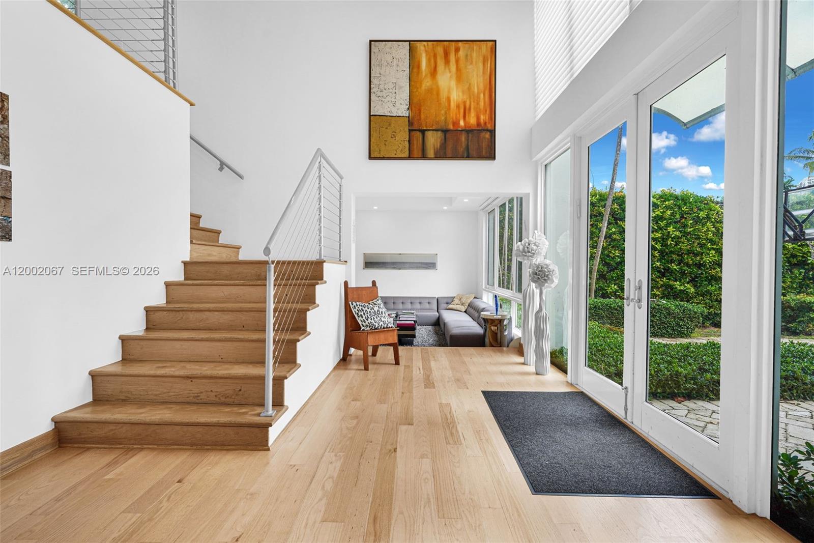 A bright entryway features light wood floors, a staircase, and a view of the outdoors — 145 Biscay Dr, Bal Harbour FL 33154, BAL HARBOUR, FL