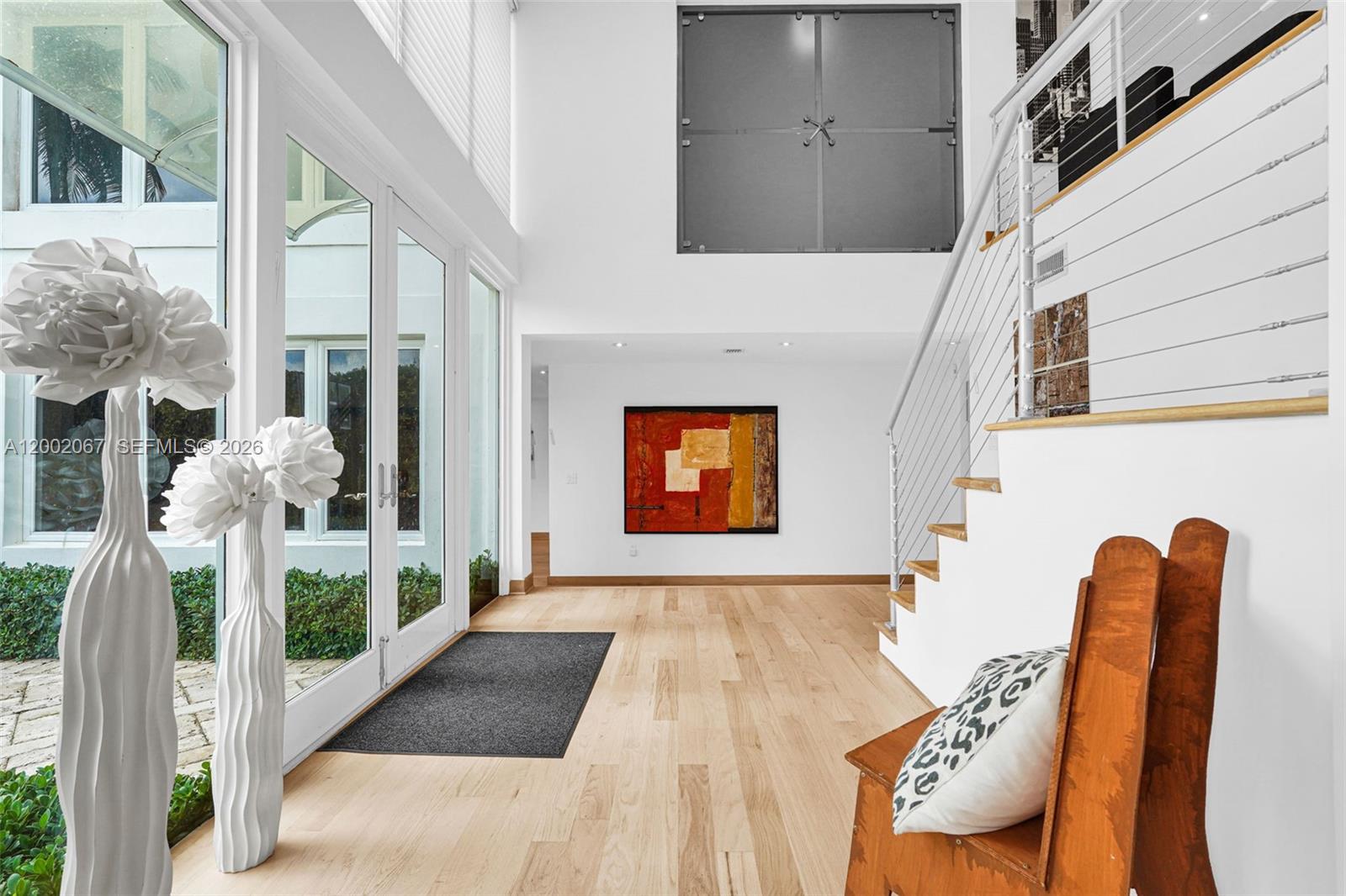 A bright entryway features light wood floors, a staircase with cable railings, and floor-to-ceiling windows — 145 Biscay Dr, Bal Harbour FL 33154, BAL HARBOUR, FL