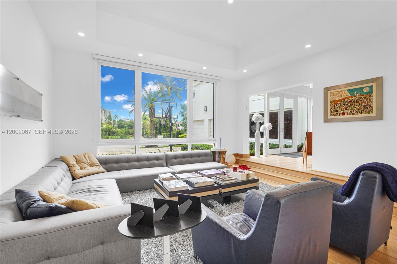 A living room features a large gray sectional, two armchairs, and a view of palm trees — 145 Biscay Dr, Bal Harbour FL 33154, BAL HARBOUR, FL