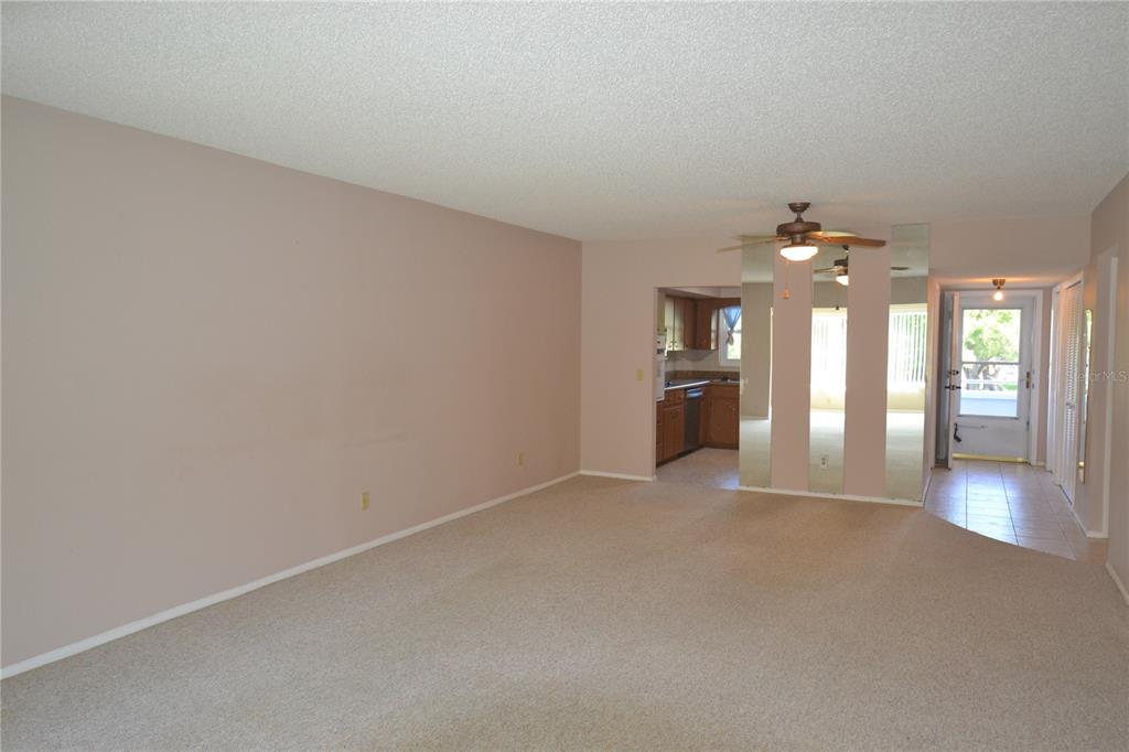 An empty living room with beige carpet, a ceiling fan, and mirrored wall panels — 2471 SUMATRAN WAY UNIT 25, CLEARWATER, FL