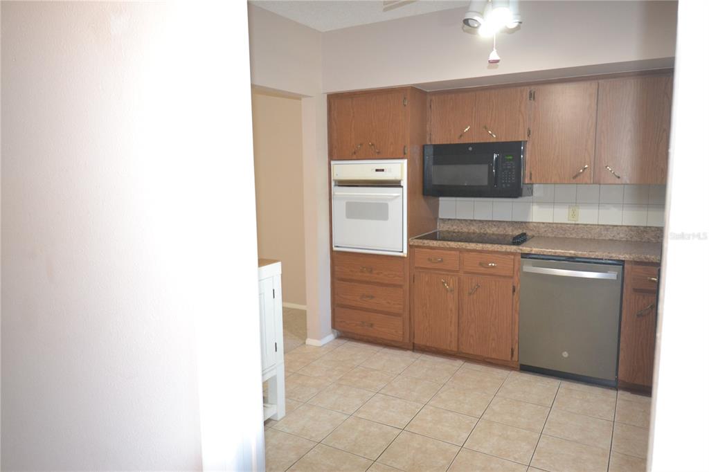 A kitchen features wood cabinets, a wall oven, a microwave, and a dishwasher — 2471 SUMATRAN WAY UNIT 25, CLEARWATER, FL