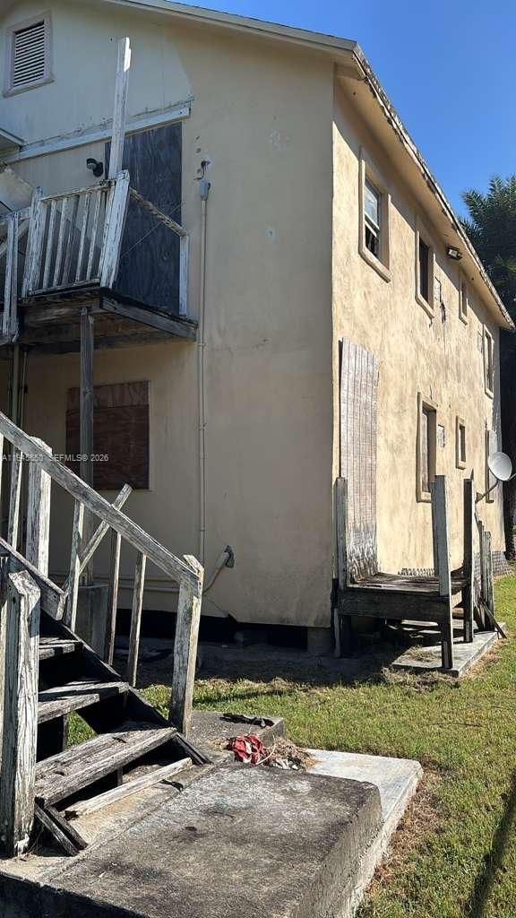 An exterior view of a weathered two-story building with boarded-up windows and wooden stairs — 263 Carissa Dr, Pahokee FL 33476, PAHOKEE, FL