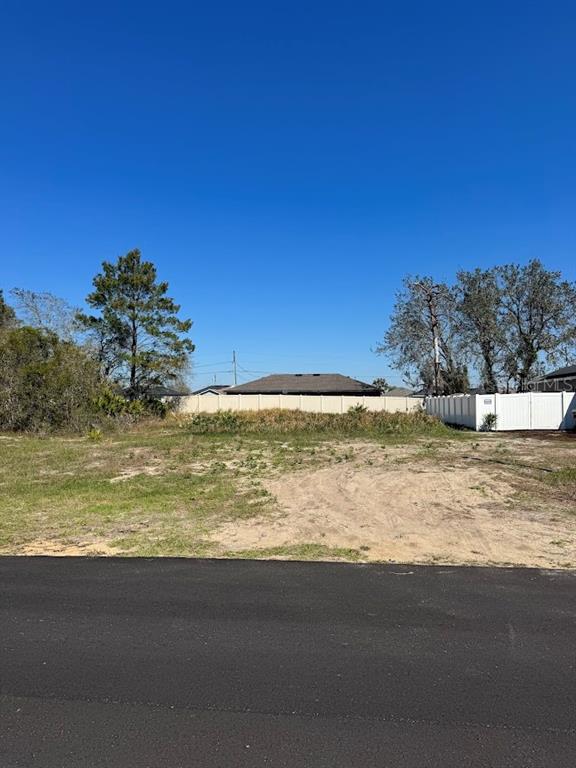 A vacant, grassy residential lot sits next to a white vinyl fence under a clear sky — 311 HIBISCUS DRIVE, POINCIANA, FL