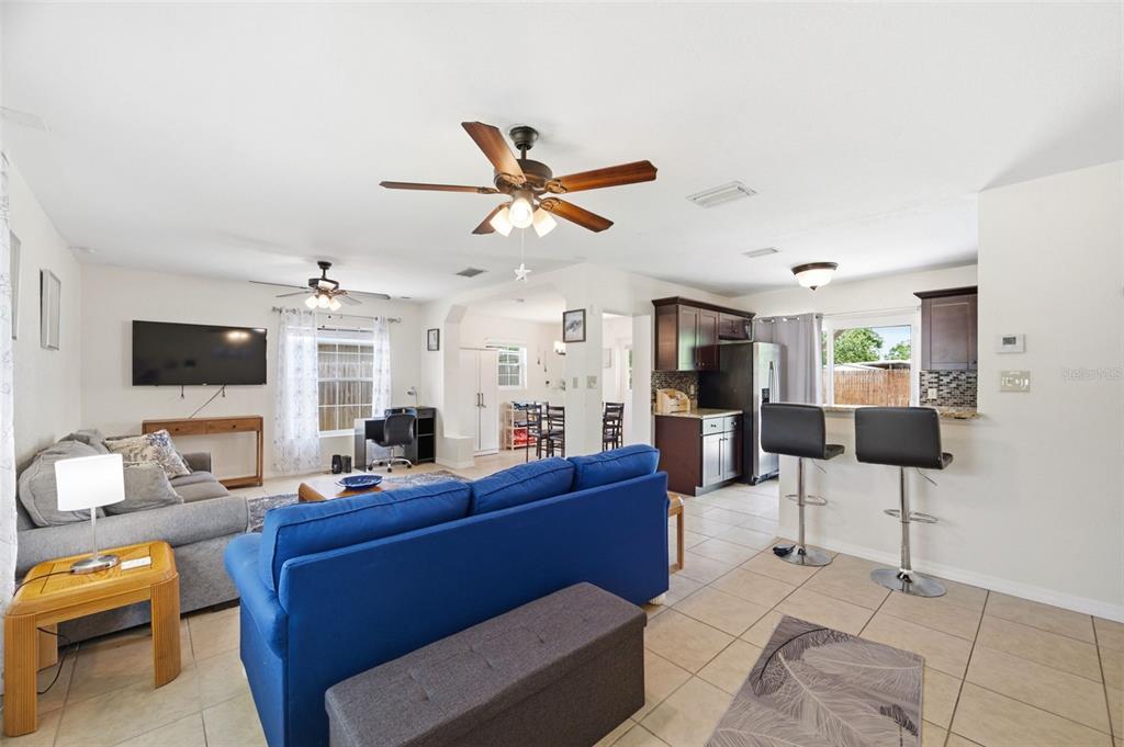 An open-concept living room and kitchen featuring a blue sofa, tile floors, and bar seating — 8685 MAGNOLIA DRIVE, SEMINOLE, FL