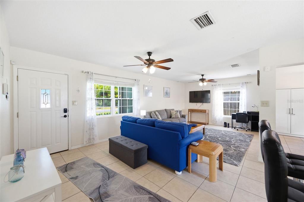 A living room features a blue sofa, tile flooring, two ceiling fans, and a desk area — 8685 MAGNOLIA DRIVE, SEMINOLE, FL