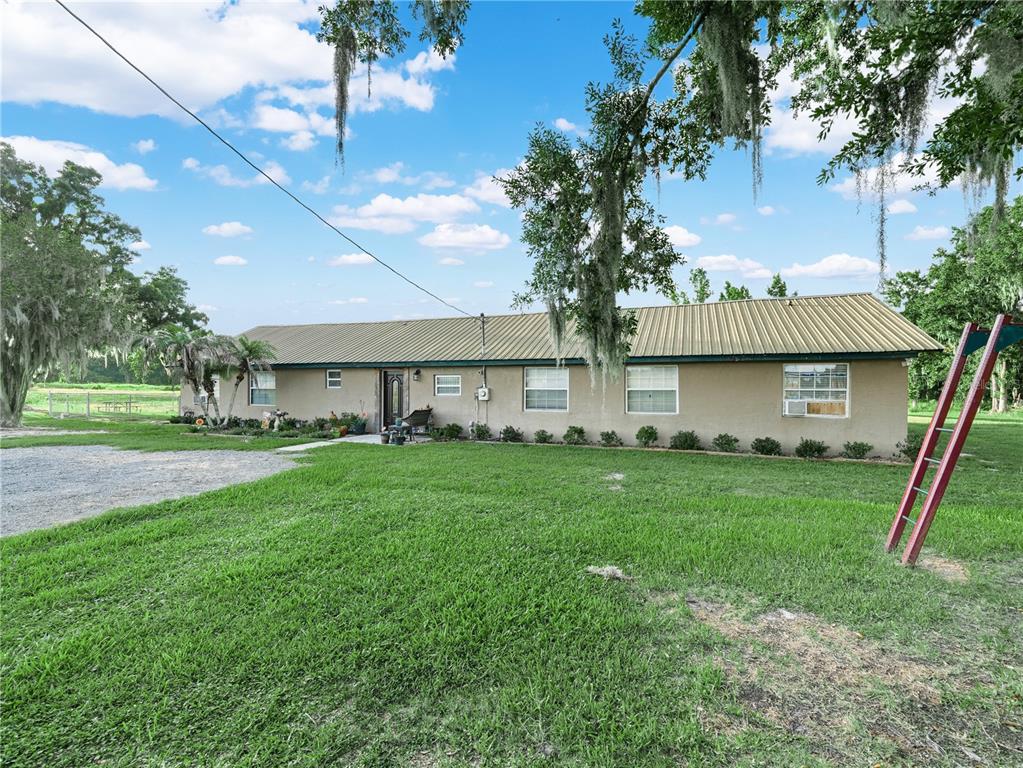 A single-story house with a metal roof and a large lawn under a cloudy sky — 702 LAKE BRANCH, BOWLING GREEN, FL