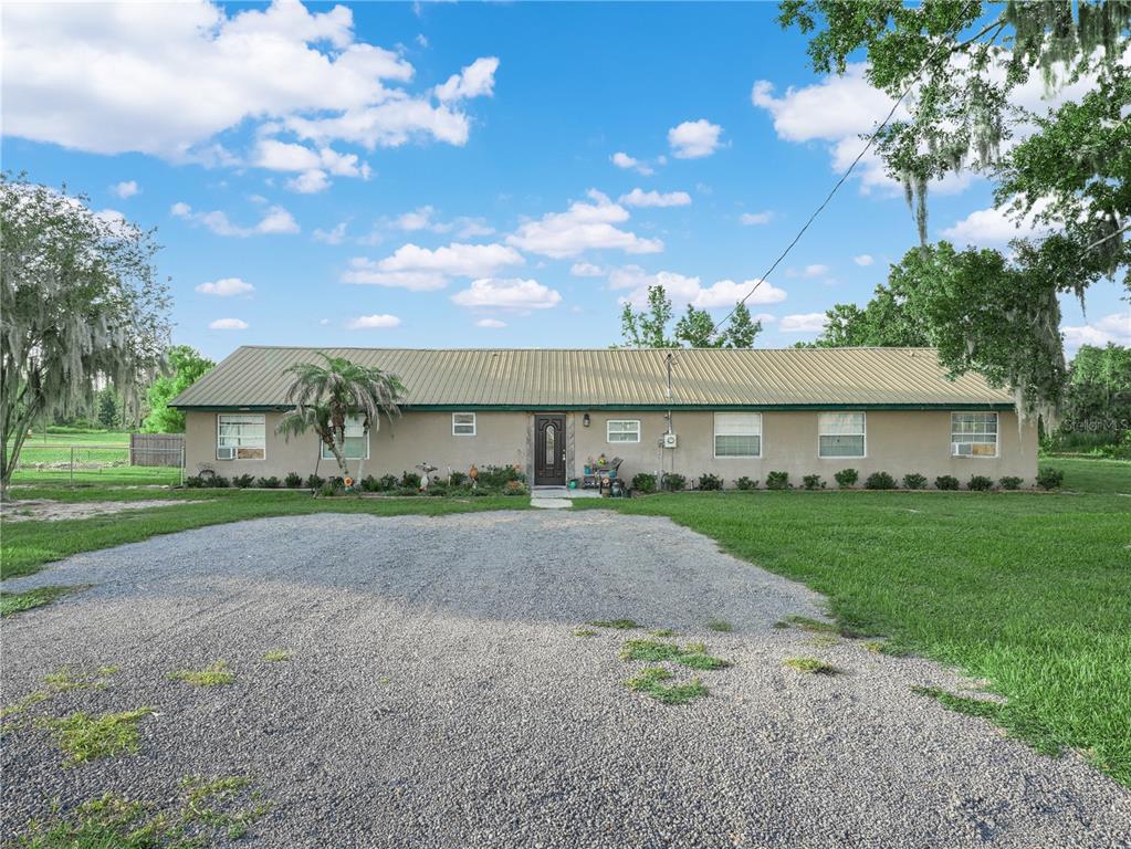 A single-story house with a metal roof and a gravel driveway in a grassy yard — 702 LAKE BRANCH, BOWLING GREEN, FL