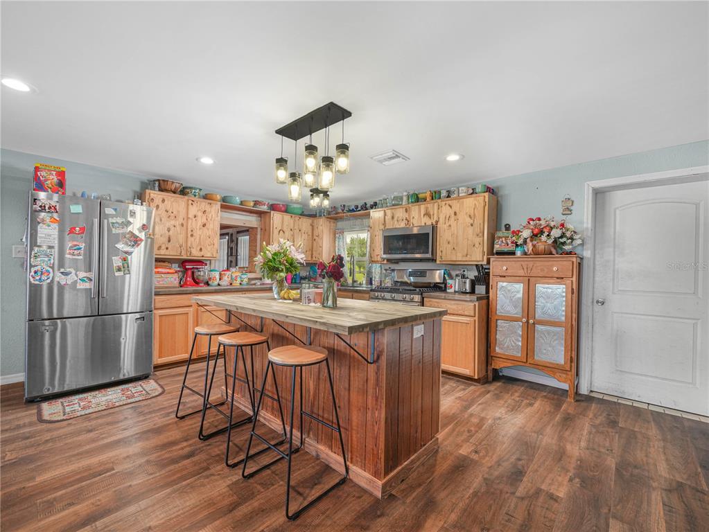 A kitchen features wood cabinets, a central island with bar stools, and stainless steel appliances — 702 LAKE BRANCH, BOWLING GREEN, FL