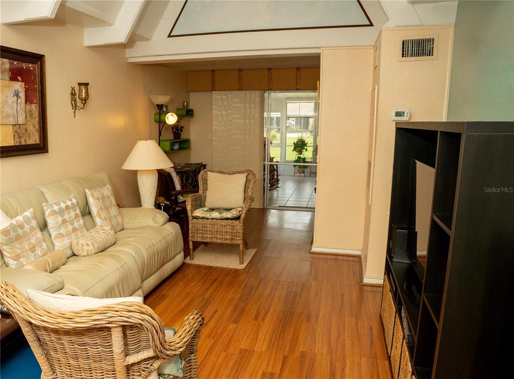 A living room features a leather sofa, wicker chairs, wood flooring, and a view into a sunroom — 1511 CLUB CIRCLE, LAKE WALES, FL