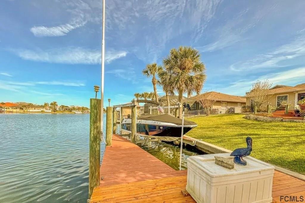 A wooden dock extends into a canal with a boat lift and a parked boat — 13 CEDARFORD COURT, PALM COAST, FL