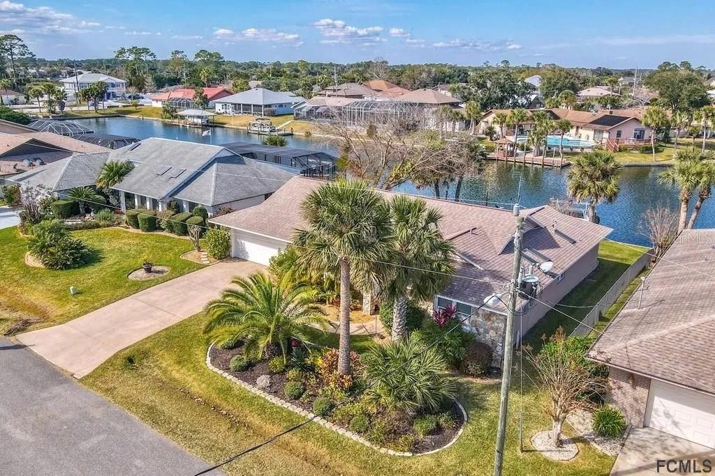 An aerial view shows a suburban house with a brown roof, palm trees, and canal access — 13 CEDARFORD COURT, PALM COAST, FL