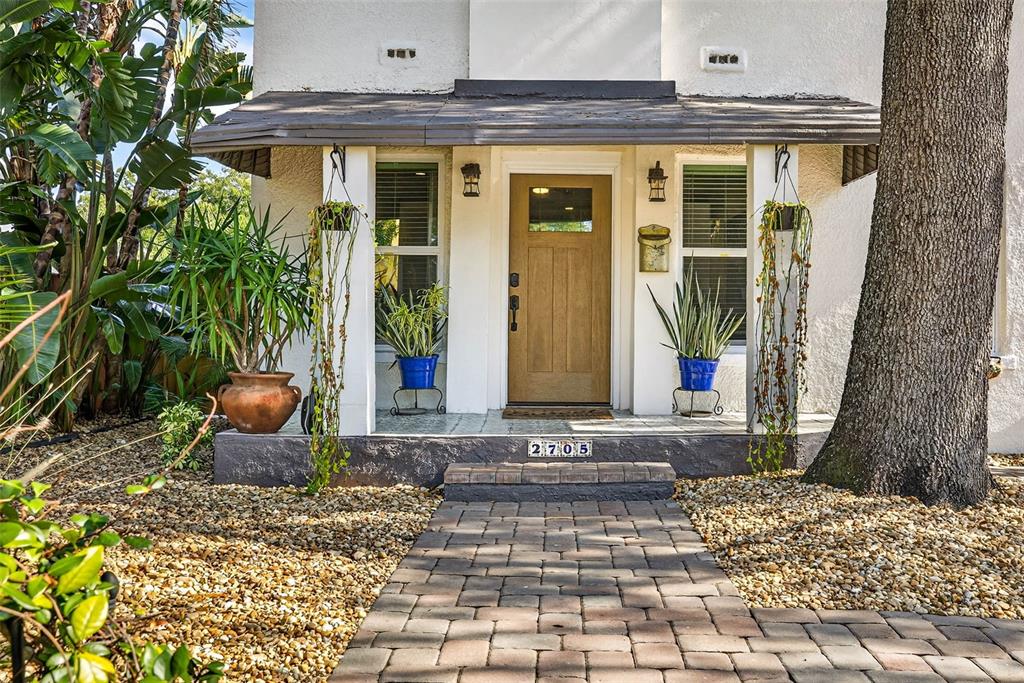 A front entrance with a wooden door, a paved walkway, and potted plants on a porch — 2705 N POPLAR AVENUE, TAMPA, FL