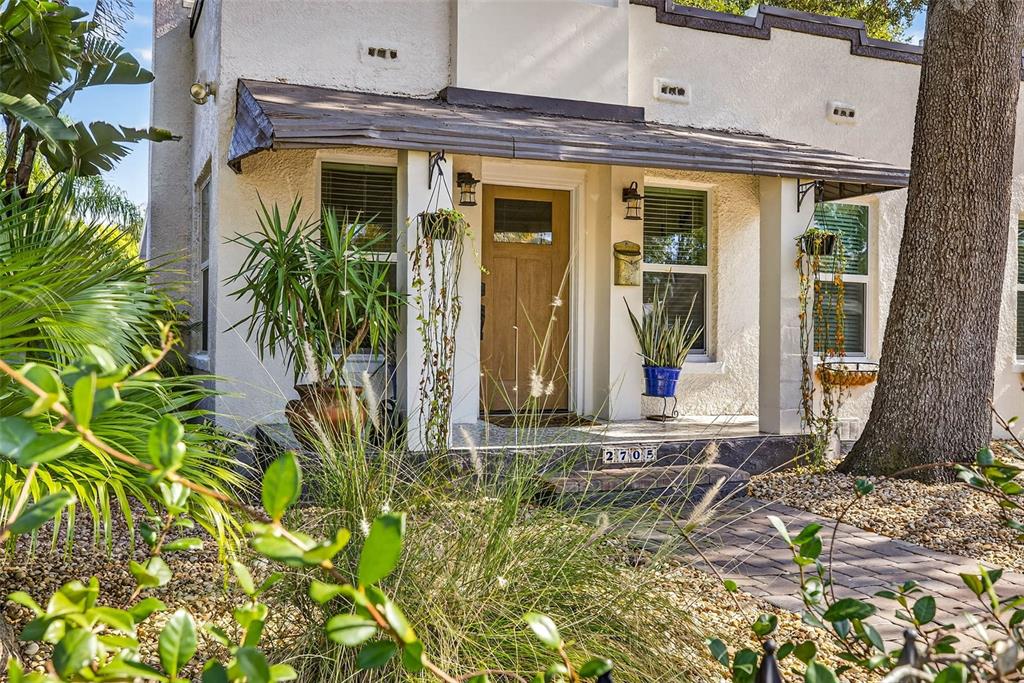 The exterior of a white stucco house features a covered porch, a wooden door, and landscaping — 2705 N POPLAR AVENUE, TAMPA, FL