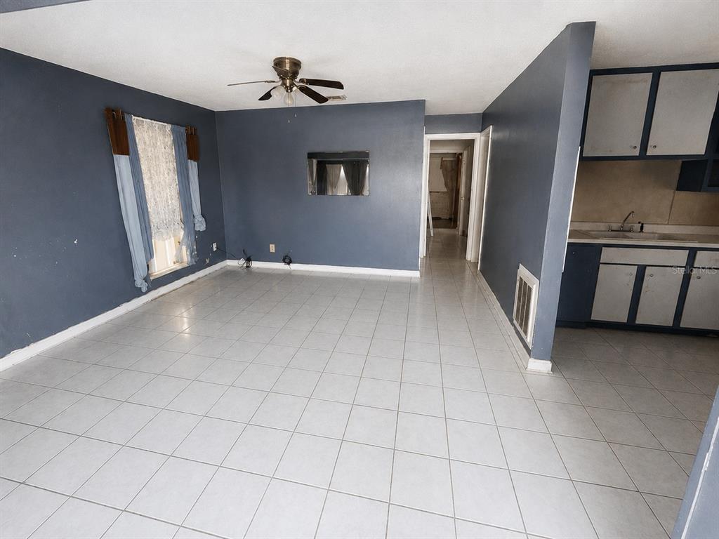 A living room with blue walls, light-colored tile flooring, a ceiling fan, and an adjacent kitchen — 48 PRINCETON AVENUE, FROSTPROOF, FL