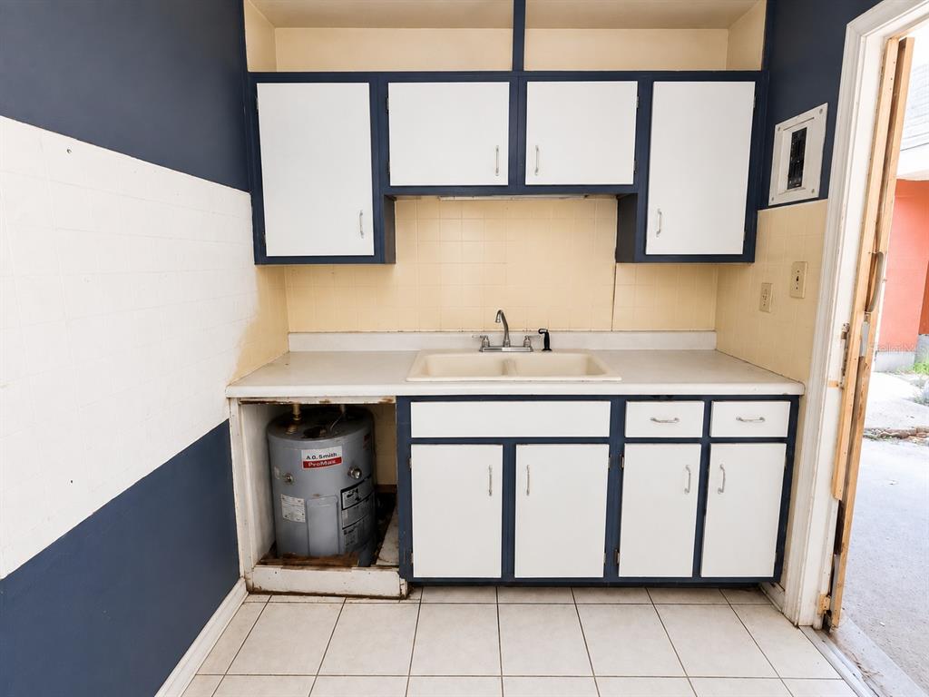 A kitchen features white cabinets with dark trim, a double sink, and an exposed water heater — 48 PRINCETON AVENUE, FROSTPROOF, FL