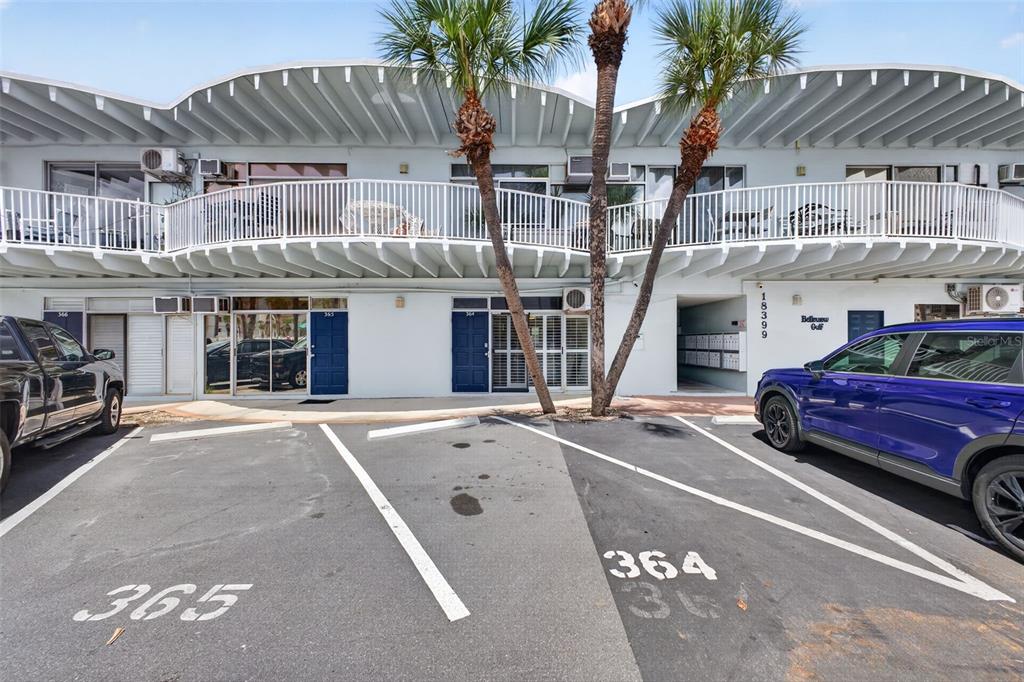 The exterior of a two-story building features a white balcony, palm trees, and parking spaces — 18399 GULF BOULEVARD UNIT 364, INDIAN ROCKS BEACH, FL