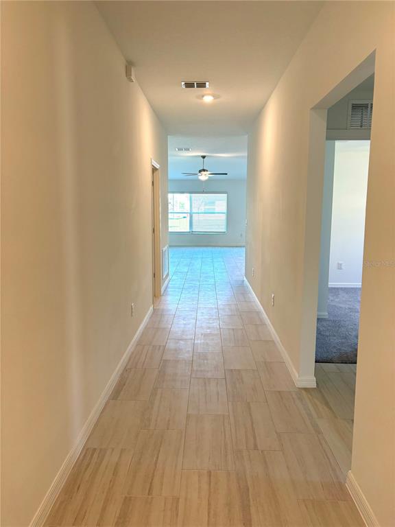 A long hallway with light-colored tile flooring leads toward a bright room with a ceiling fan — 3615 NATURAL TRACE STREET, PLANT CITY, FL