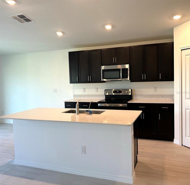 A kitchen features dark wood cabinets, white countertops, a central island, and stainless steel appliances — 3615 NATURAL TRACE STREET, PLANT CITY, FL