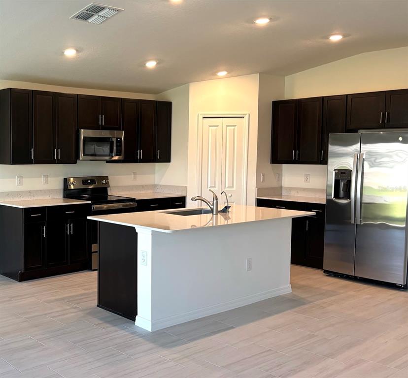 A kitchen features dark wood cabinets, white countertops, a central island, and stainless steel appliances — 3615 NATURAL TRACE STREET, PLANT CITY, FL