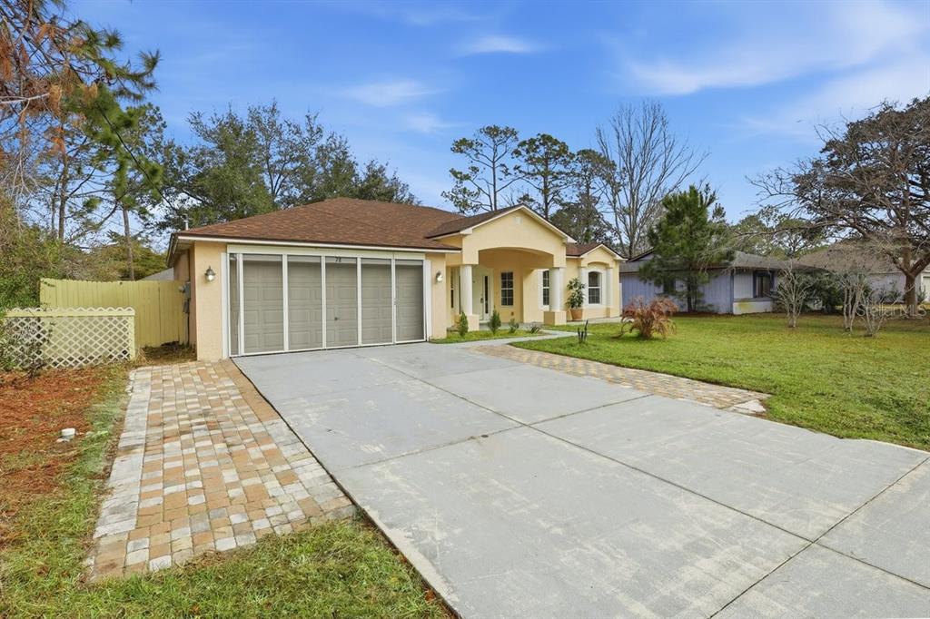 A single-story house with a beige exterior, a concrete driveway, and a screened-in garage door — 78 PANORAMA, PALM COAST, FL