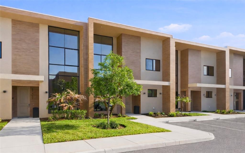 A modern two-story townhouse exterior with wood-look siding, large glass windows, and a paved parking lot — 7455 BROOKLYN DRIVE, KISSIMMEE, FL