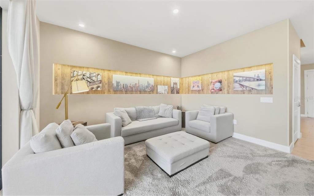 A living room features light gray furniture, a central ottoman, and a wood-paneled accent wall — 7455 BROOKLYN DRIVE, KISSIMMEE, FL
