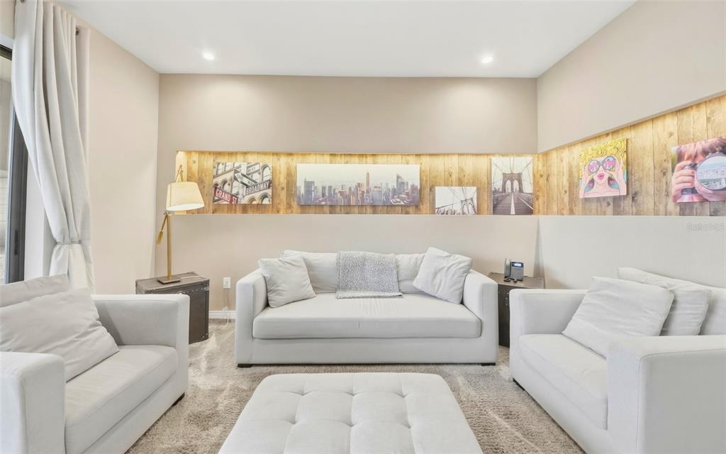 A living room features white sofas, a matching ottoman, and a wood-paneled wall with artwork — 7455 BROOKLYN DRIVE, KISSIMMEE, FL