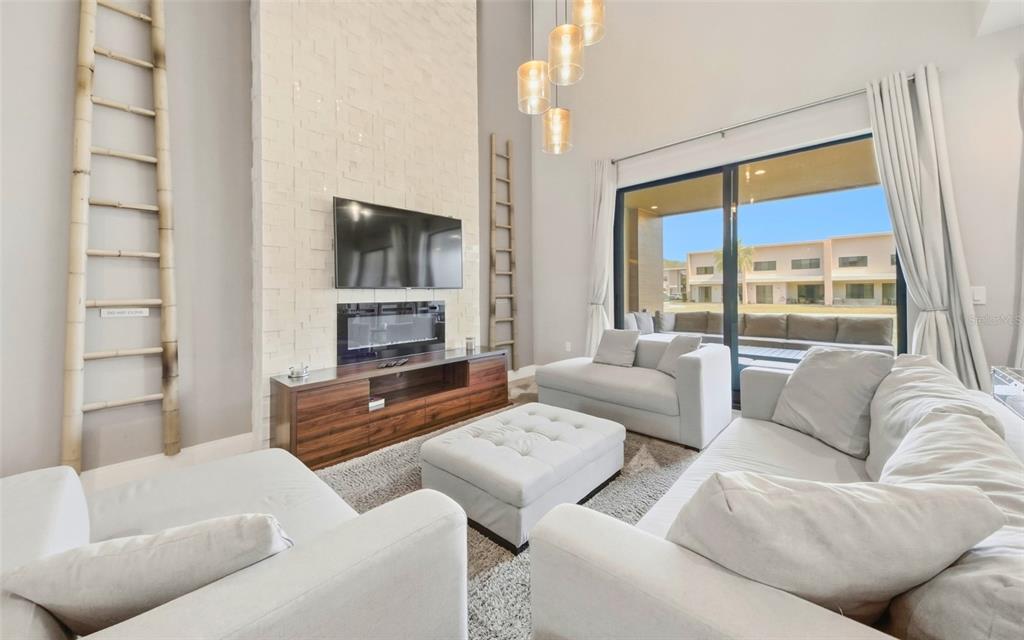 A living room features a tall stone fireplace, a wall-mounted television, and large sliding doors — 7455 BROOKLYN DRIVE, KISSIMMEE, FL