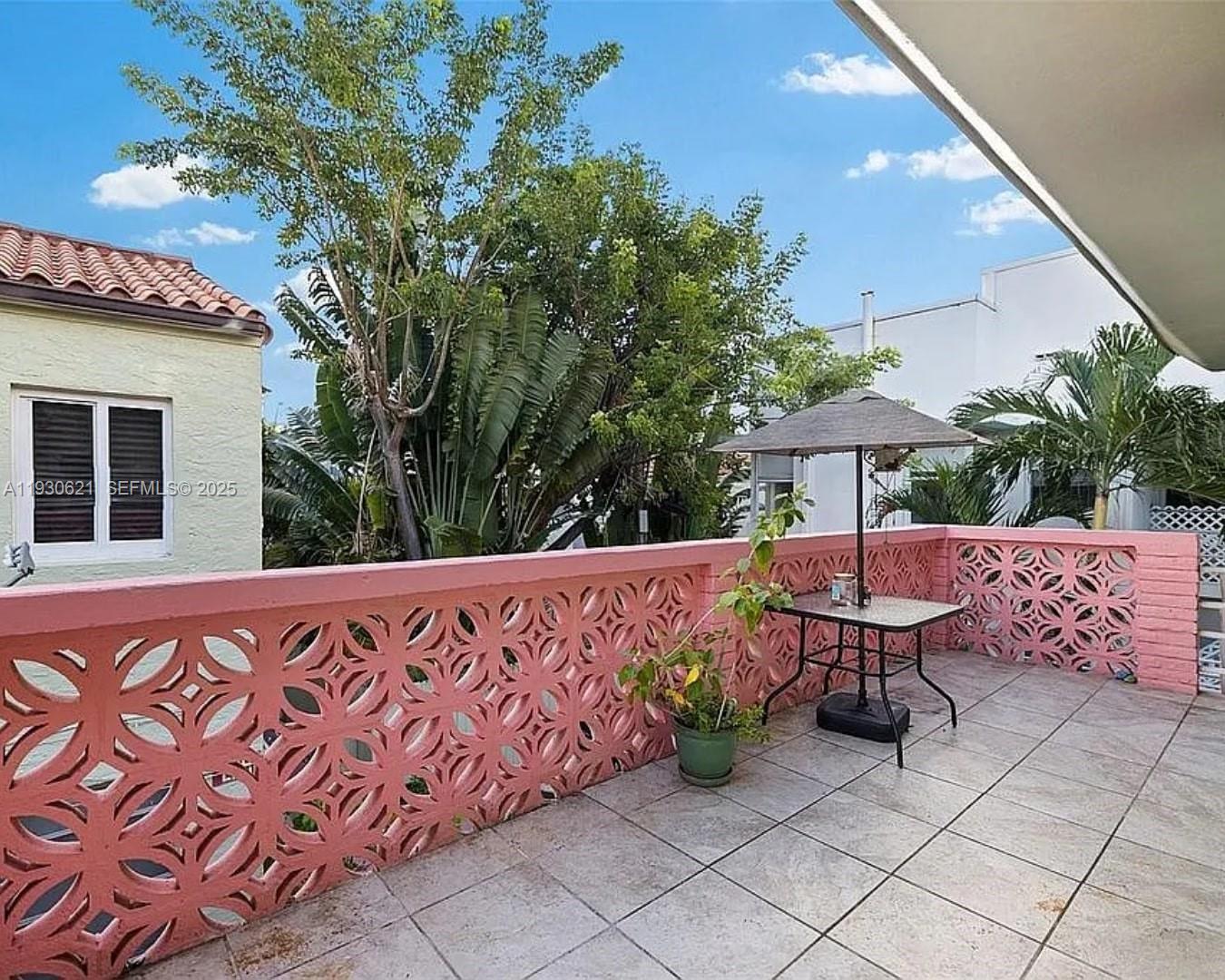 A tiled outdoor balcony features a pink decorative breeze block railing and a patio table — 2822 Pine Tree Dr, Miami Beach FL 33140, MIAMI BEACH, FL