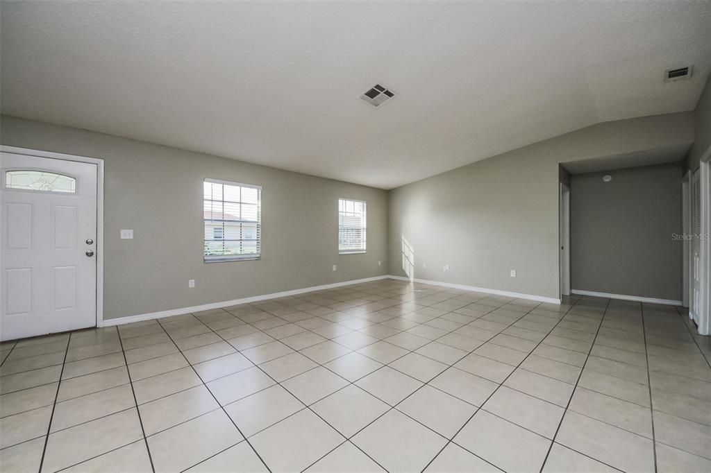 A spacious living room features light-colored tile flooring, neutral walls, and two windows — 211 COBALT DRIVE, KISSIMMEE, FL