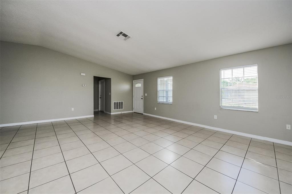 A spacious living room features light gray walls, white trim, and large beige floor tiles — 211 COBALT DRIVE, KISSIMMEE, FL