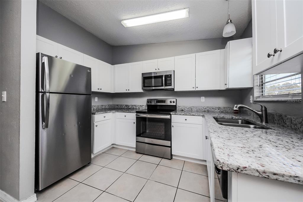 A kitchen features white cabinets, stainless steel appliances, and granite countertops with tile flooring — 211 COBALT DRIVE, KISSIMMEE, FL