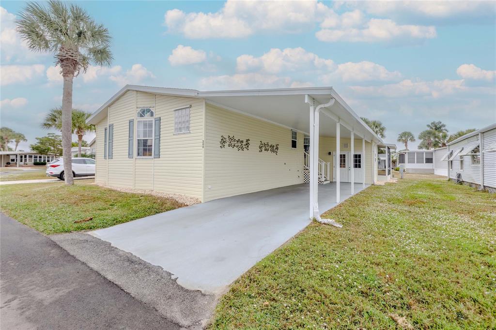 A light yellow manufactured home features a long concrete carport and a palm tree nearby — 2100 KINGS HIGHWAY UNIT 200, PORT CHARLOTTE, FL