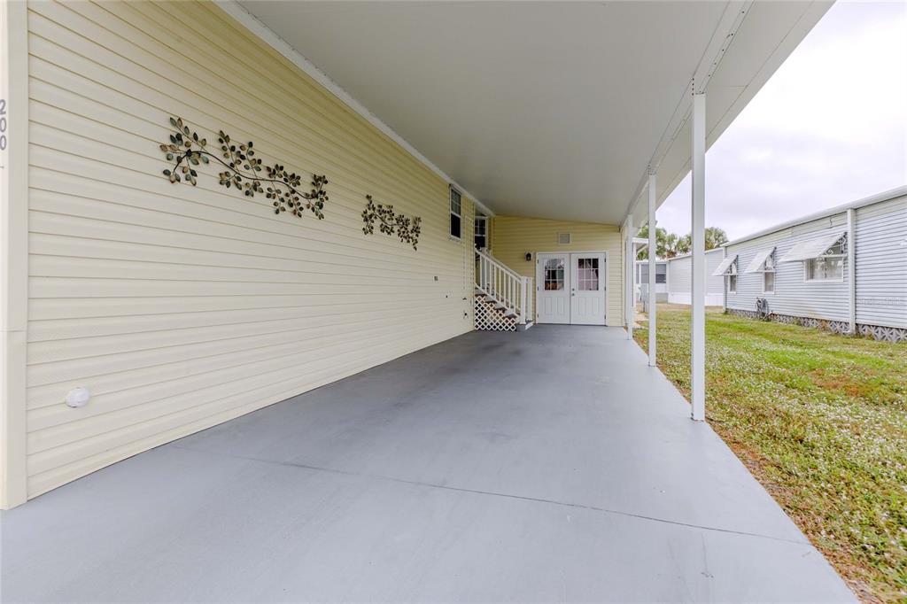 A long, covered concrete carport runs alongside the light yellow siding of a mobile home — 2100 KINGS HIGHWAY UNIT 200, PORT CHARLOTTE, FL