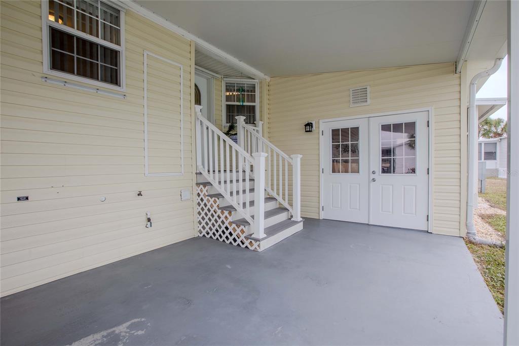 A covered patio features light yellow siding, a set of white stairs, and double doors — 2100 KINGS HIGHWAY UNIT 200, PORT CHARLOTTE, FL