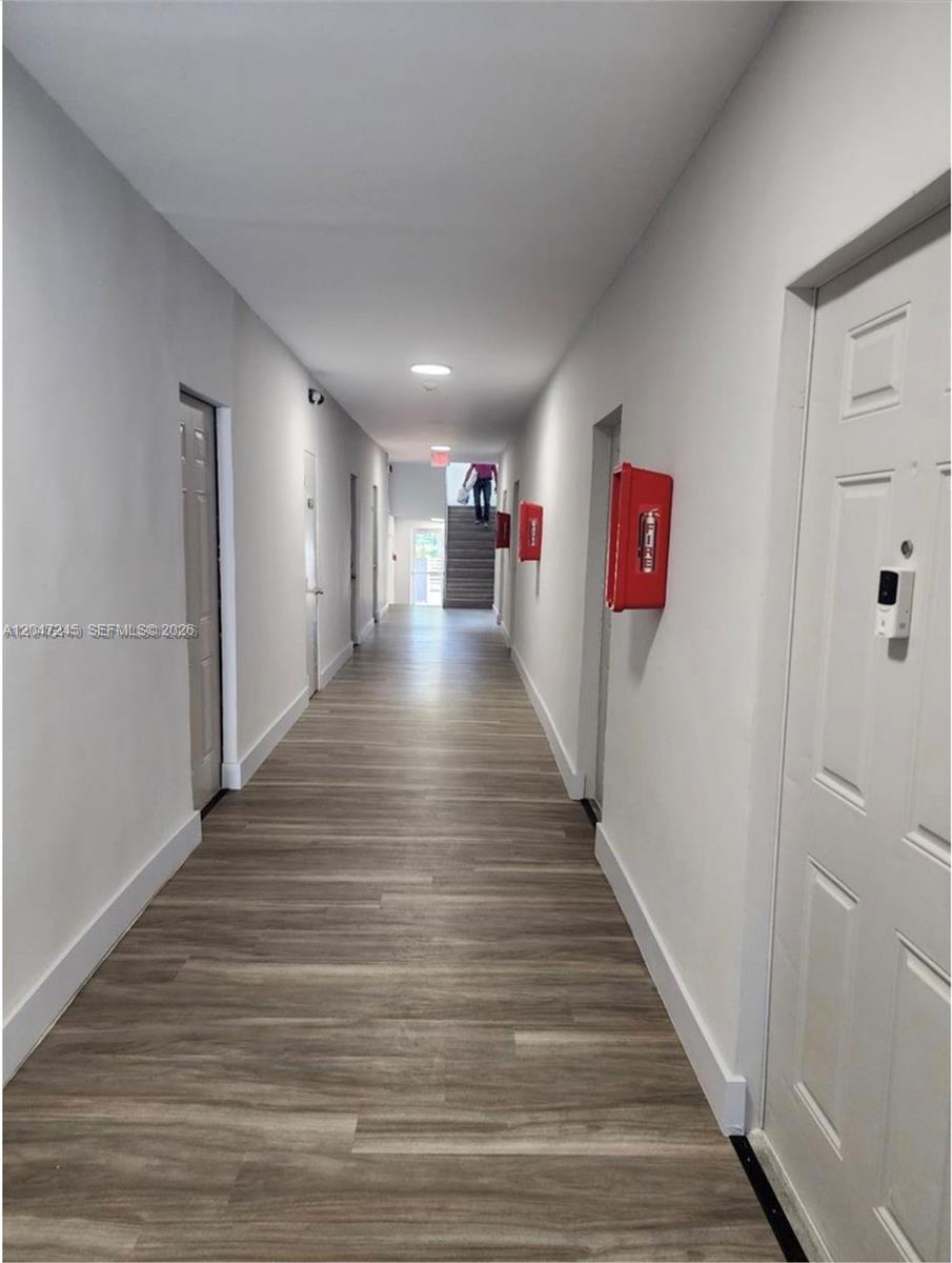 A long indoor hallway features light wood-look flooring, white walls, and red fire extinguisher cabinets — 852 SW 13th Ave # 3, Miami FL 33135, MIAMI, FL