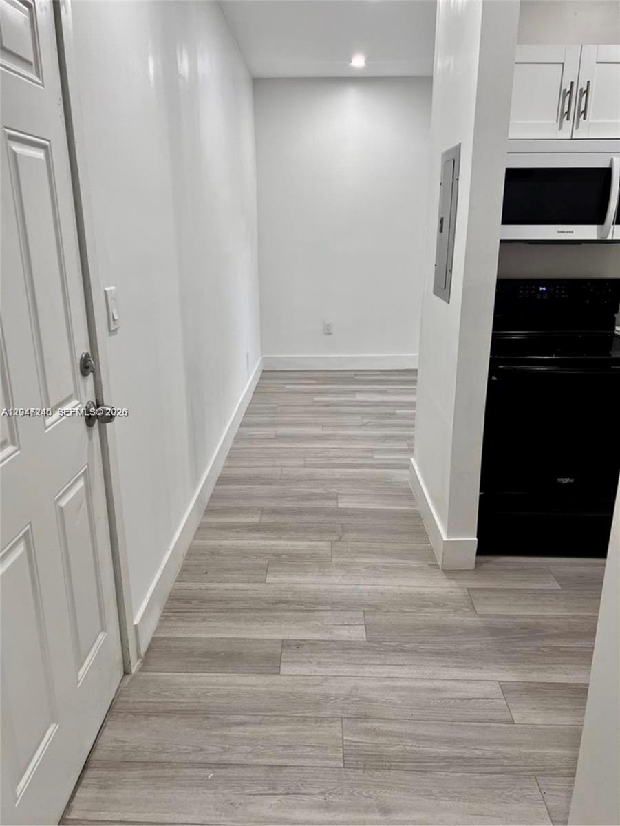 A narrow hallway with light wood-look flooring leads to a kitchen with black appliances — 852 SW 13th Ave # 3, Miami FL 33135, MIAMI, FL