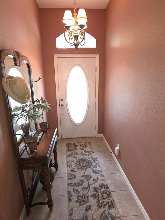 An entryway features a white front door, a wooden console table with a mirror, and a chandelier — 11442 TURTLE DOVE PLACE, NEW PORT RICHEY, FL