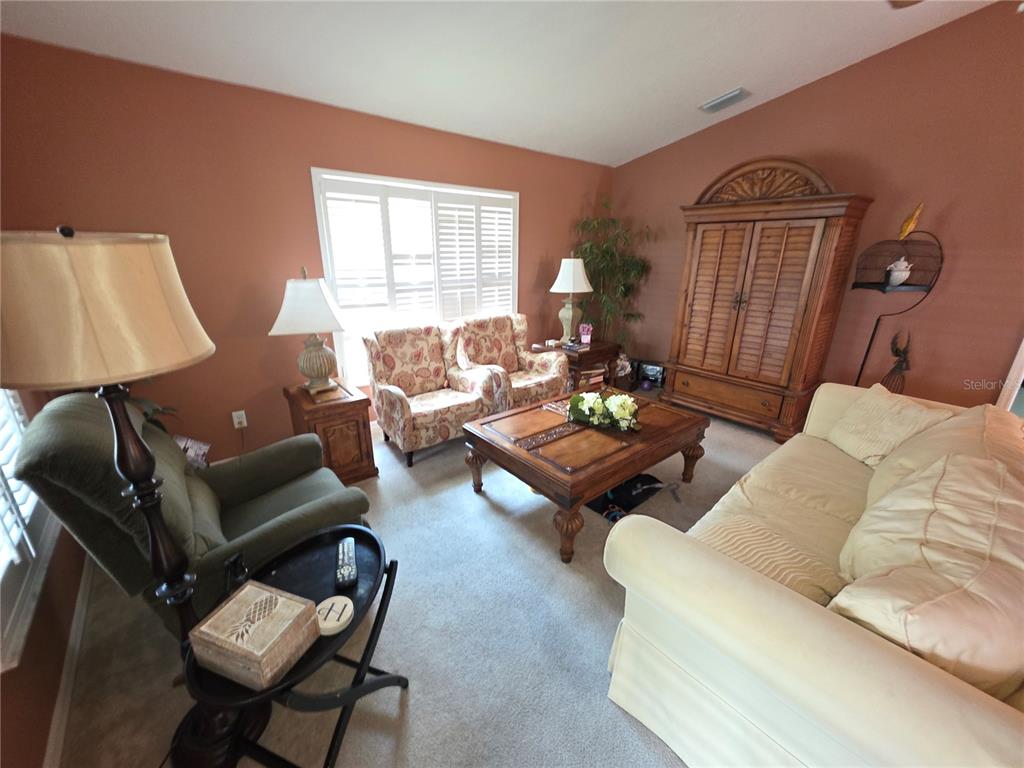 A living room features a beige sofa, two patterned armchairs, a wooden coffee table, and an armoire — 11442 TURTLE DOVE PLACE, NEW PORT RICHEY, FL