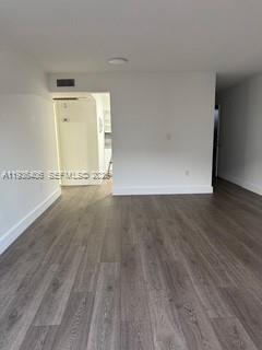 An empty room with gray wood-look flooring and white walls leads toward a kitchen area — 2460 SW 18th Ave # 1211, Miami FL 33145, MIAMI, FL