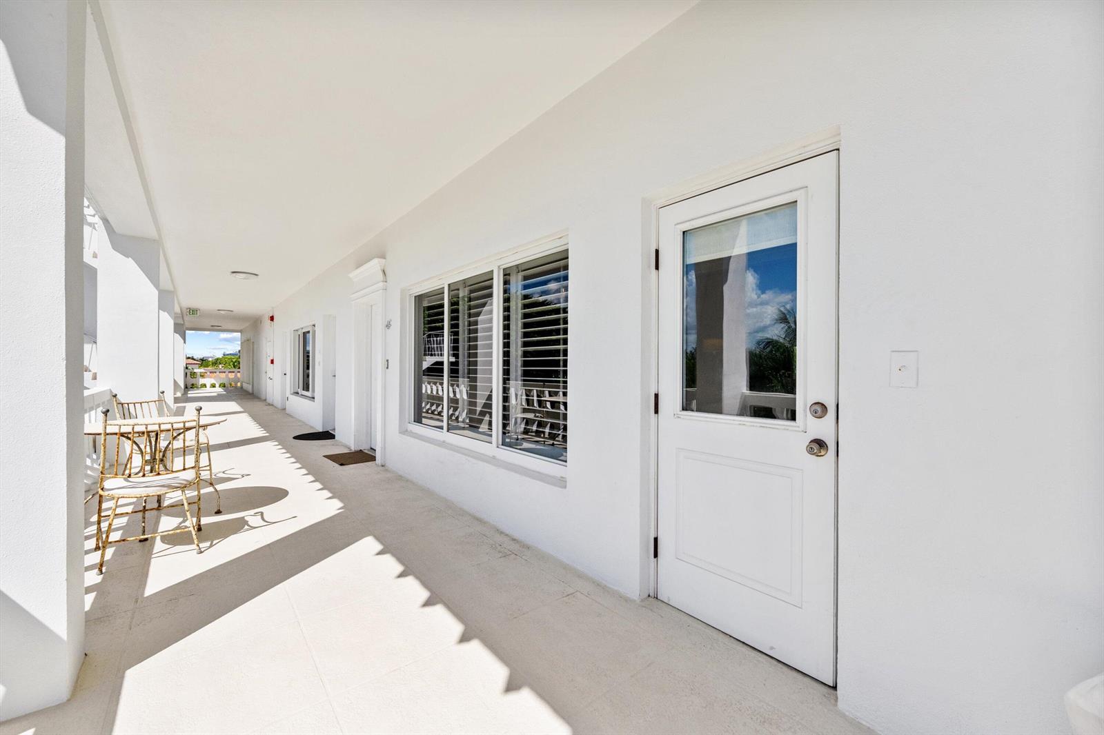 A white exterior hallway features a glass-paneled door, large windows, and a small patio set — 300 S Ocean Boulevard # 4f, Palm Beach FL 33480, PALM BEACH, FL