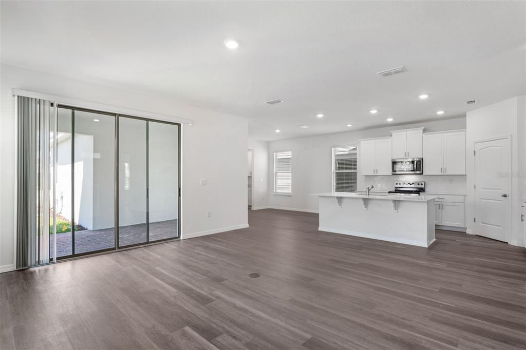 An open-concept kitchen and living area featuring white cabinets, a center island, and wood-look flooring — 12032 SHINE VIEW LANE, WINTER GARDEN, FL